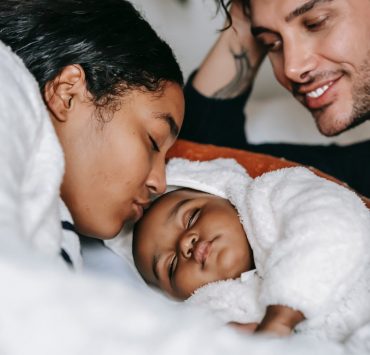 cheerful young multiethnic parents admiring sleeping baby on bed