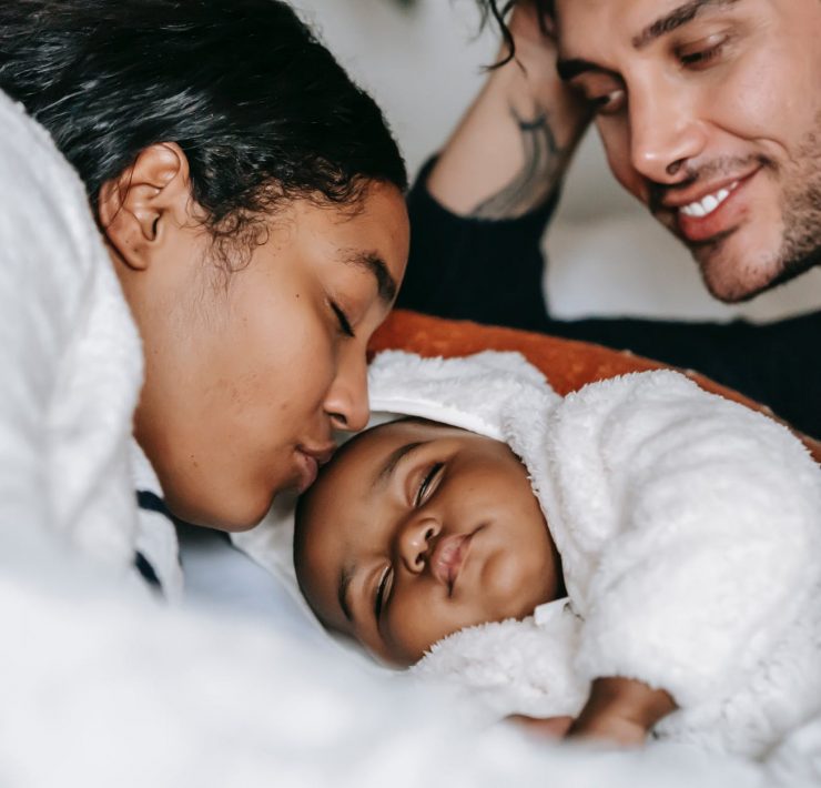 cheerful young multiethnic parents admiring sleeping baby on bed