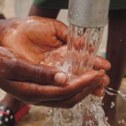 close up of a child s hands catching water from the spout of a water pump