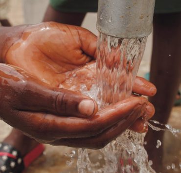 close up of a child s hands catching water from the spout of a water pump
