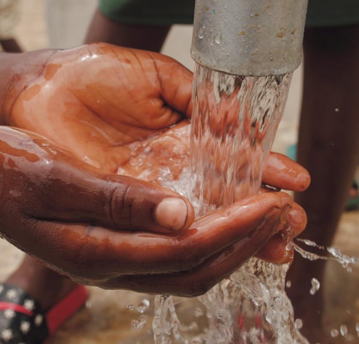 close up of a child s hands catching water from the spout of a water pump