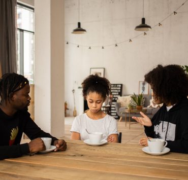 black parents lecturing upset daughter at table