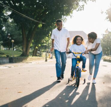 man standing beside his wife teaching their child how to ride bicycle