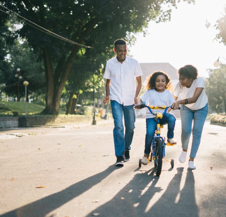 man standing beside his wife teaching their child how to ride bicycle