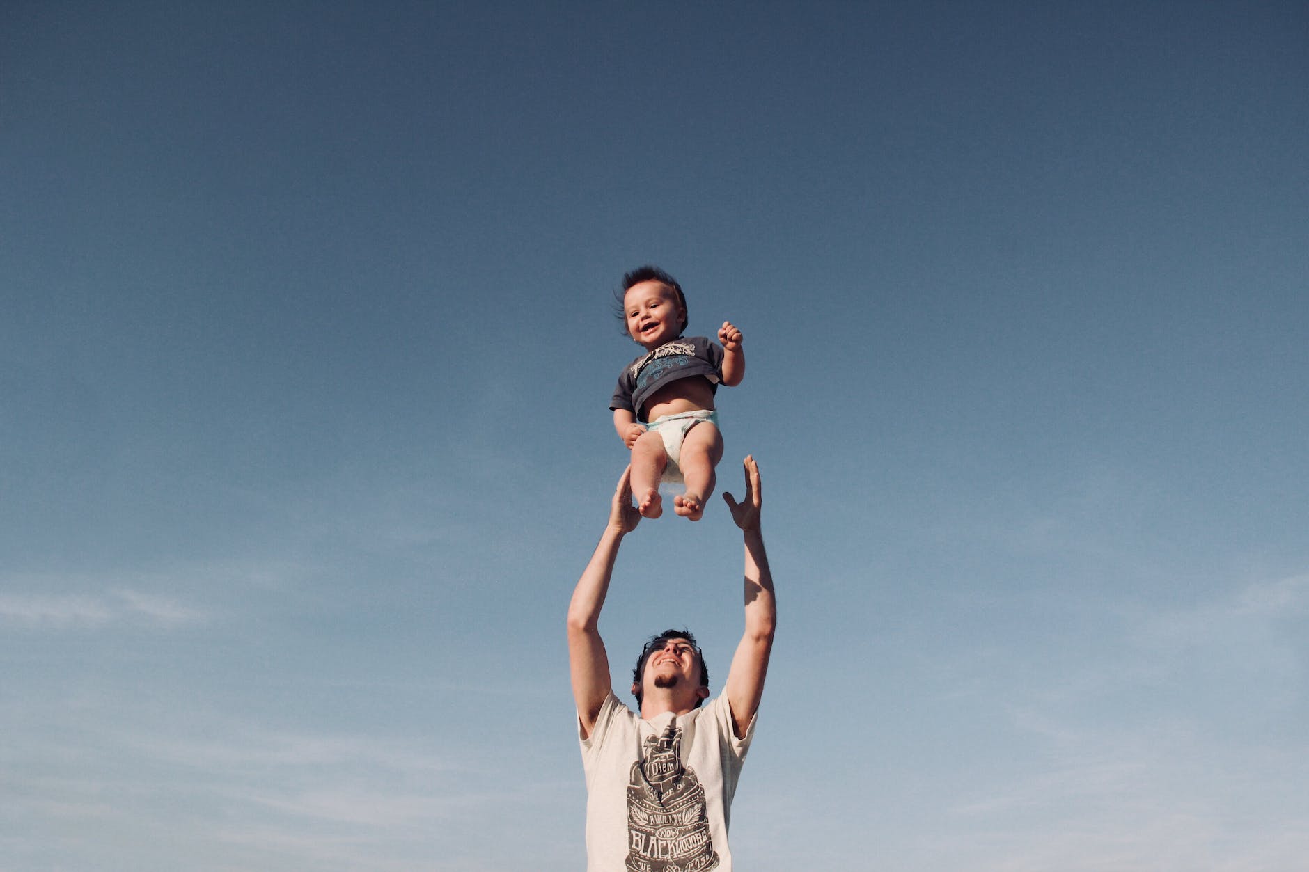 photo of man in raising baby under blue sky