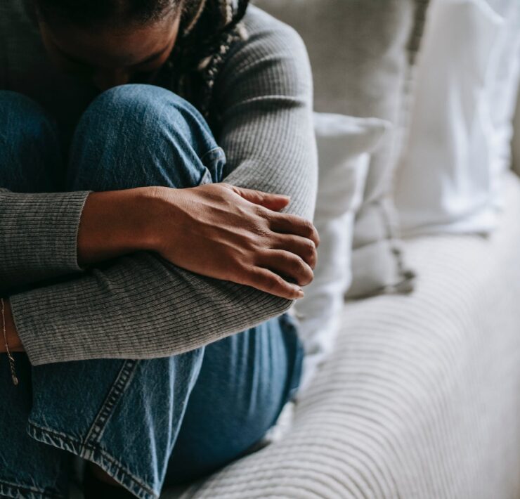 crop pitiful black woman embracing knees on bed